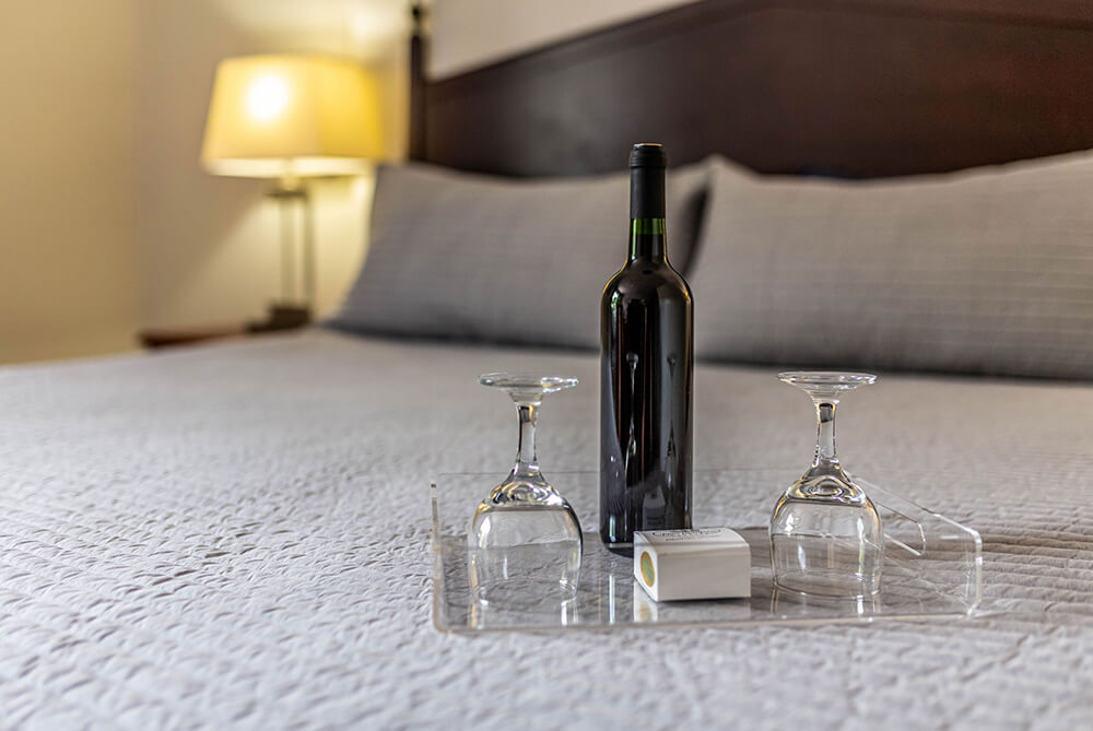Bottle of wine and glasses in a tray on a bed.